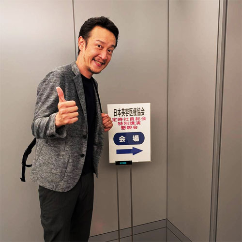 日本美容医療協会、会場案内の前でポーズをとる柏崎
